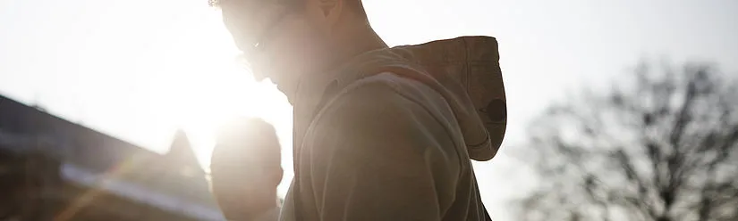 Two students are standing on campus in the evening sun, their faces are hardly recognizable