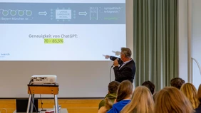 A man with a microphone looks and points to a presentation. 