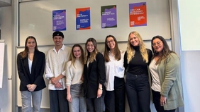 Seven people smiling into the camera, four posters hanging behind them.