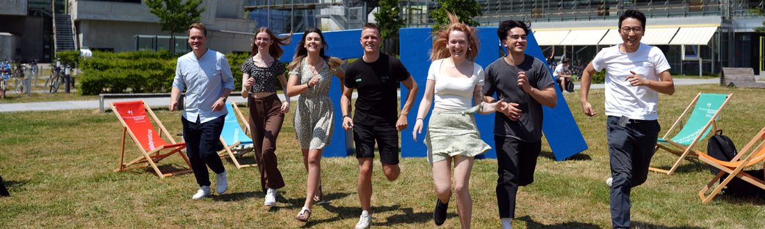 Studierende laufen auf der Campuswiese in einer Reihe Richtung Kamera