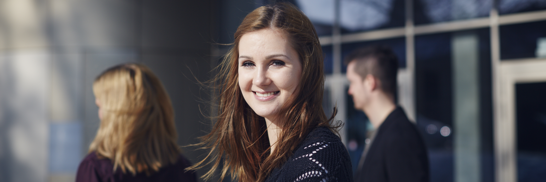 A female student smiles into the camera, in the background two other students