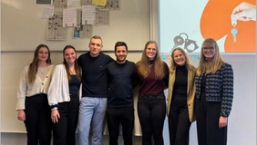 Seven people smile into the camera, with sales ads hanging on a board behind them.