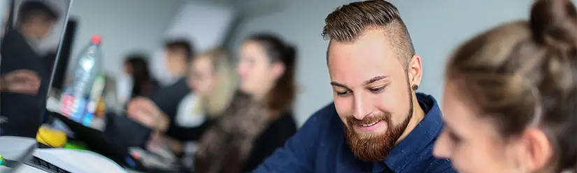 Zwei Studenten besprechen sich im Hörsaal zu Studieninhalten; im Hintergrund weitere Studenten