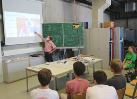 Professor zeigt auf die Bildschirmpräsentation im Hörsaal vor den Schülern