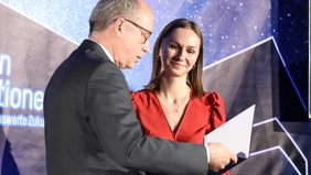 Woman in a red dress receives a cheque from a man.