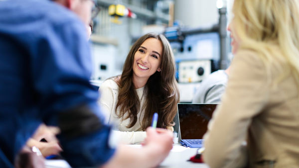 Students talk to each other. They sit at a table in a laboratory of the THI.