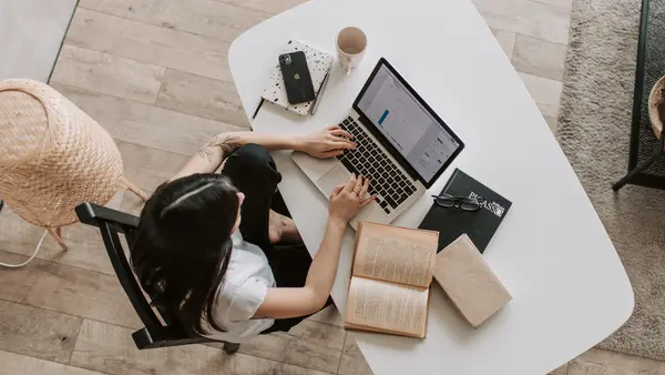 Eine Studentin sitzt mit Laptop und Büchern an einen Tisch