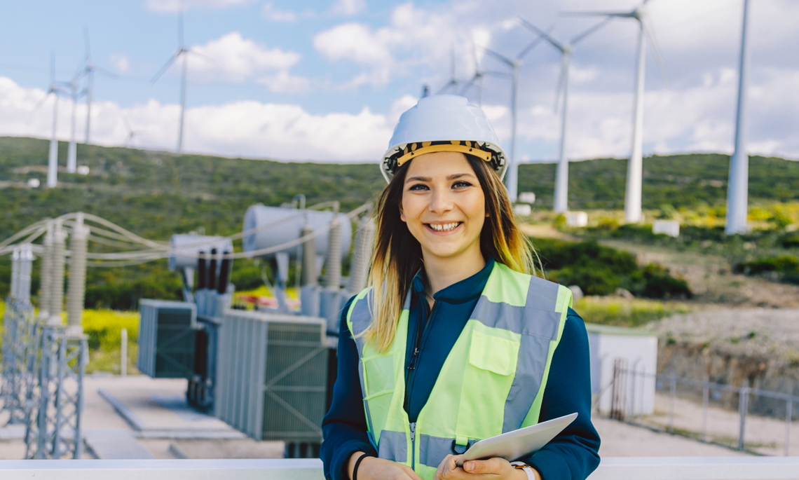 Frau mit Bauhelm vor Windrädern