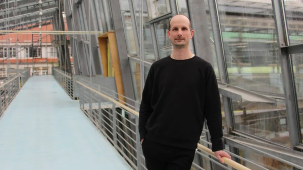 A man dressed in dark clothes in a glass stairwell.