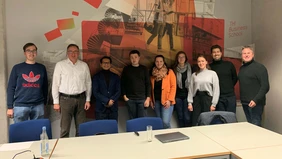 9 people in a meeting room in front of a modern wall.