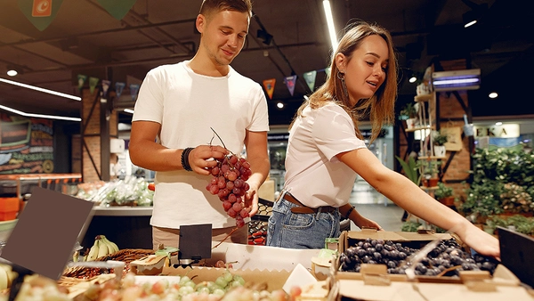 A young man and a woman standing in a supermarket holding grapes in their hands