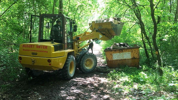 Bagger füllt einen Müllcontainer im Wald