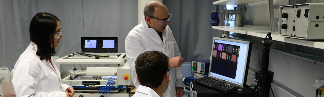 Three scientists in white coats look at a screen in the laboratory