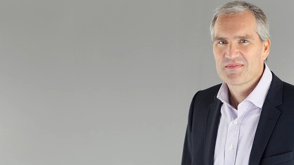 Prof. Dr. Marc Knoppe in a dark suit in front of a gray background