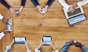 [Translate to English:] Image of hands on a wooden table working with smartphones, tablets or notebooks.